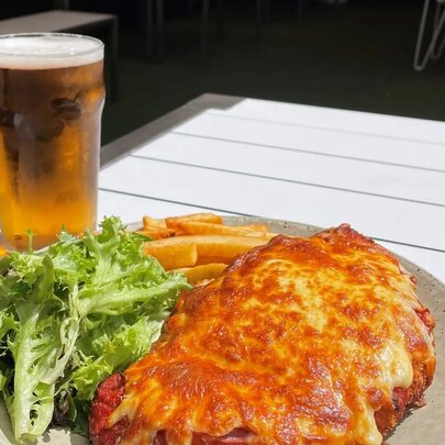 A plate of chicken parma, with salad and chips, and a pint of beer on an outdoor table at a pub.