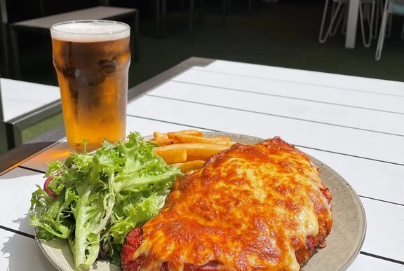 A plate of chicken parma, with salad and chips, and a pint of beer on an outdoor table at a pub.