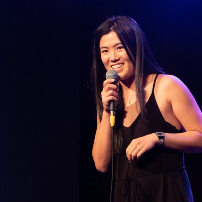 Comedian Annie Louey on stage holding a microphone.
