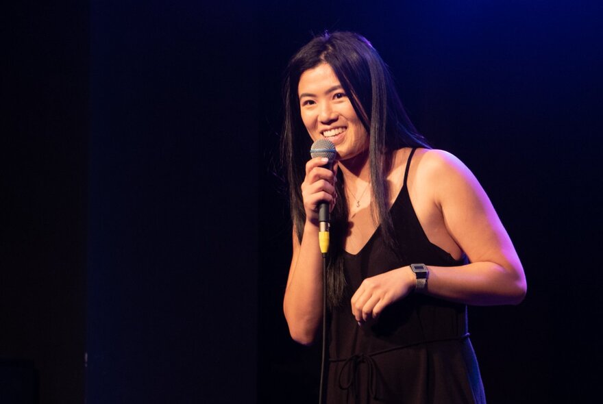 Comedian Annie Louey on stage holding a microphone.