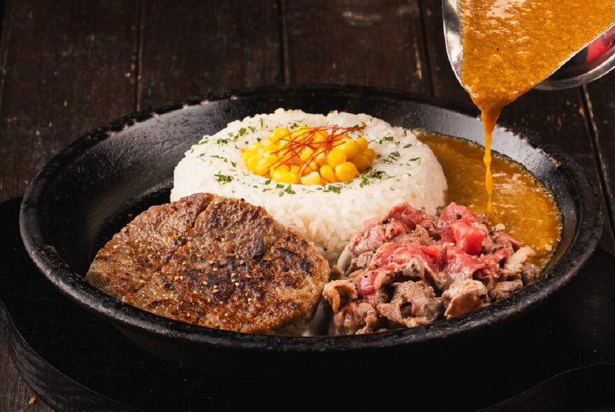 A dish of pepper steak with a side of rice, and sauce being poured from a jug.