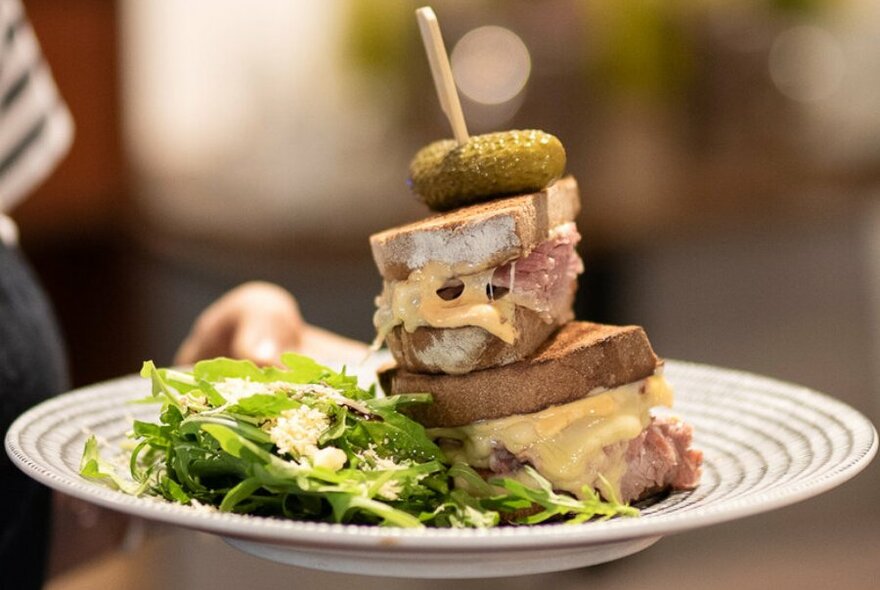 A cafe meal with a stack of Rueben sandwich and a green salad.