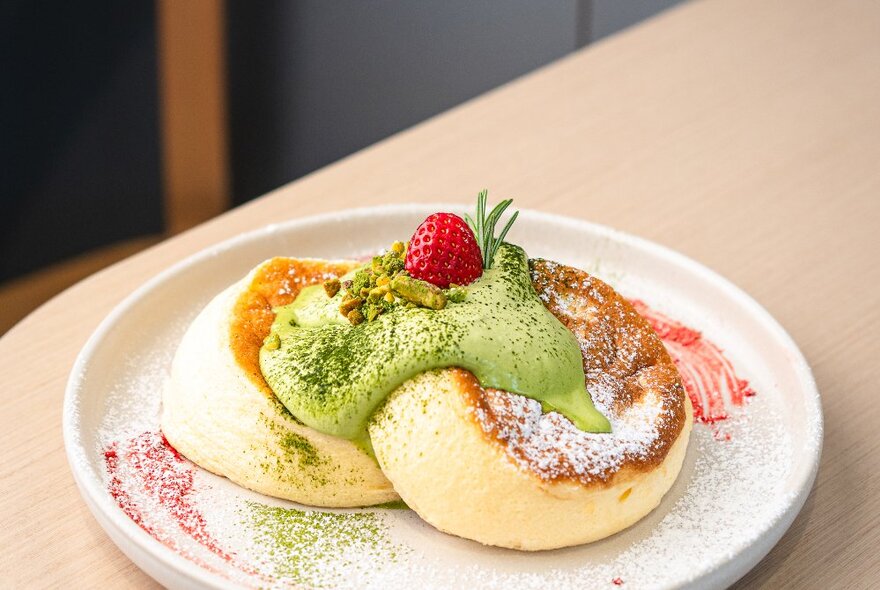 Souffle-style fluffy pancakes on a plate with matcha sauce and a strawberry. 