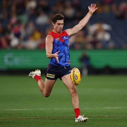 A Melbourne AFL player running while about to kick a yellow football he has just dropped in front of his leg.
