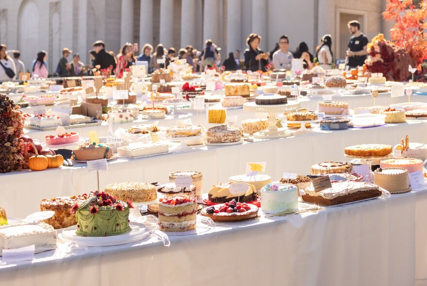 People queueing at tables topped with many many homemade cakes.