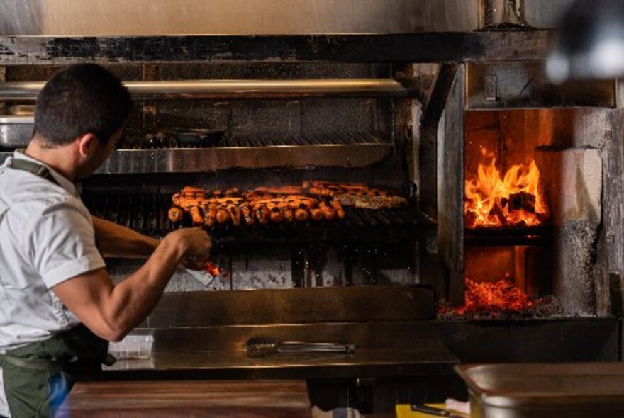 Chef placing trays of meat in an oven next to a wood-fired stove.