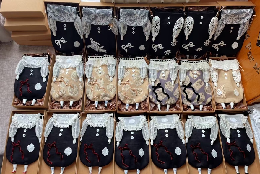 A collection of small hand-made dolls displayed in cardboard boxes and lined up next to each other in three rows.
