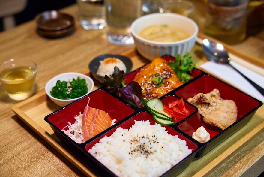 A bento box with miso soup and condiments. 