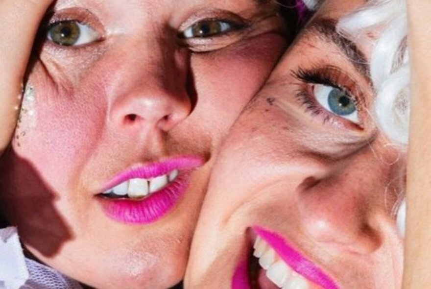 Two faces in close-up, squashed close together, both wearing hot pink lipstick.