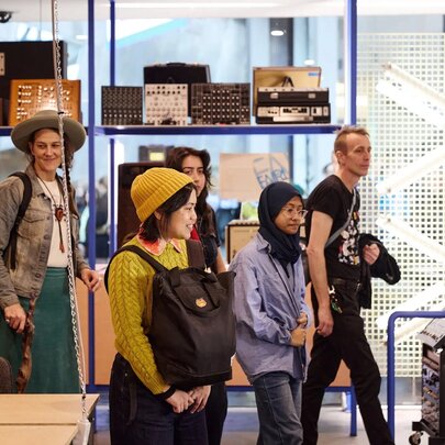 Visitors on a tour at the Melbourne Electronic Sound Studio with electronic instruments on display on shelves. 