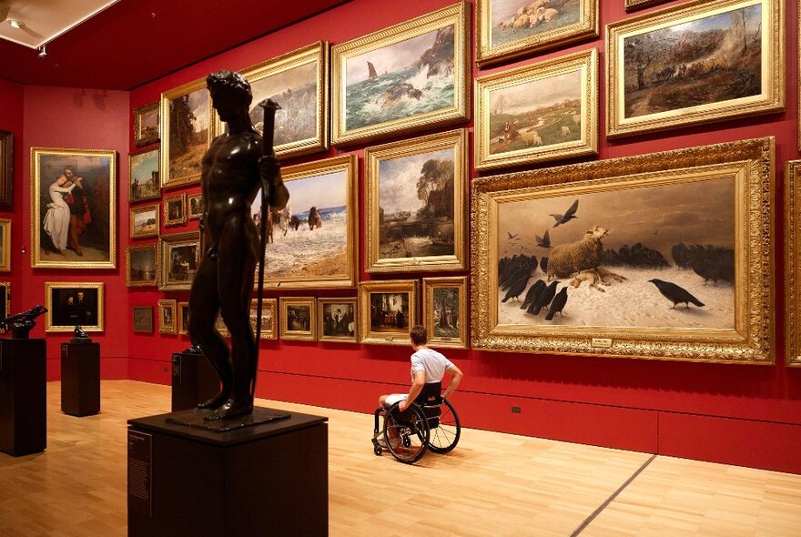 A person in a wheelchair is looking at paintings in a gallery.