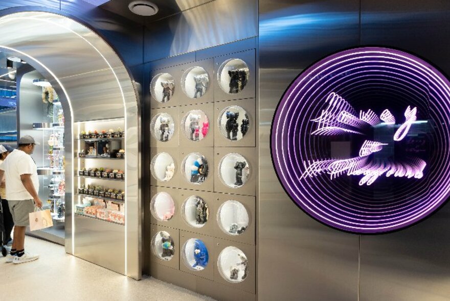 Sleek stainless steel interior of retail cafe space with people looking at displays of collectible toys and objects encased in a wall.