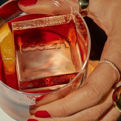 A hand holding a cocktail that has an ice cube that says Society.