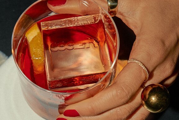 A hand holding a cocktail that has an ice cube that says Society.