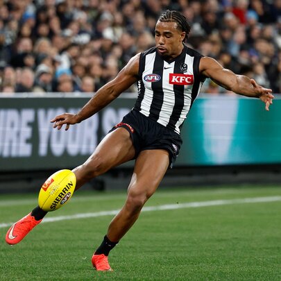 A Collingwood Magpies AFL player kicking a yellow football during a game.