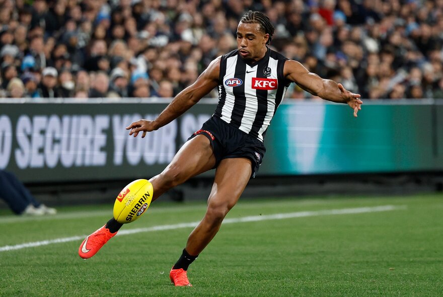 A Collingwood Magpies AFL player kicking a yellow football during a game.