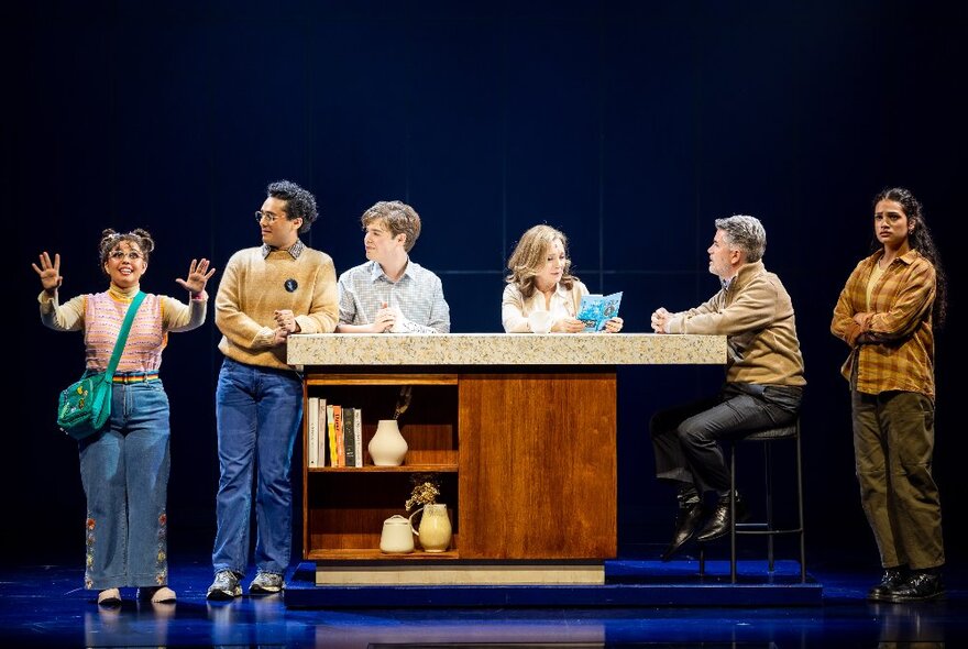 A cast of actors performing with props and sets on a theatre stage. 