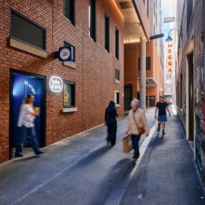 A Melbourne city laneway, with blurred pedestrians walking along it and past the exterior of BakeStand, a small bakery.