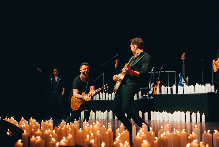 Two musicians playing guitar on a candlelit stage.