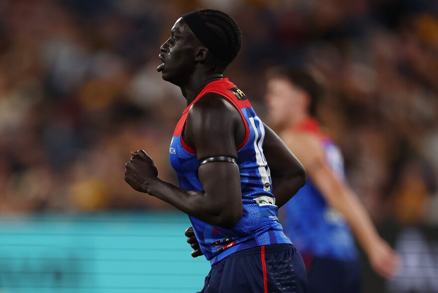 A Melbourne AFL football player in profile, running on the ground during a match.