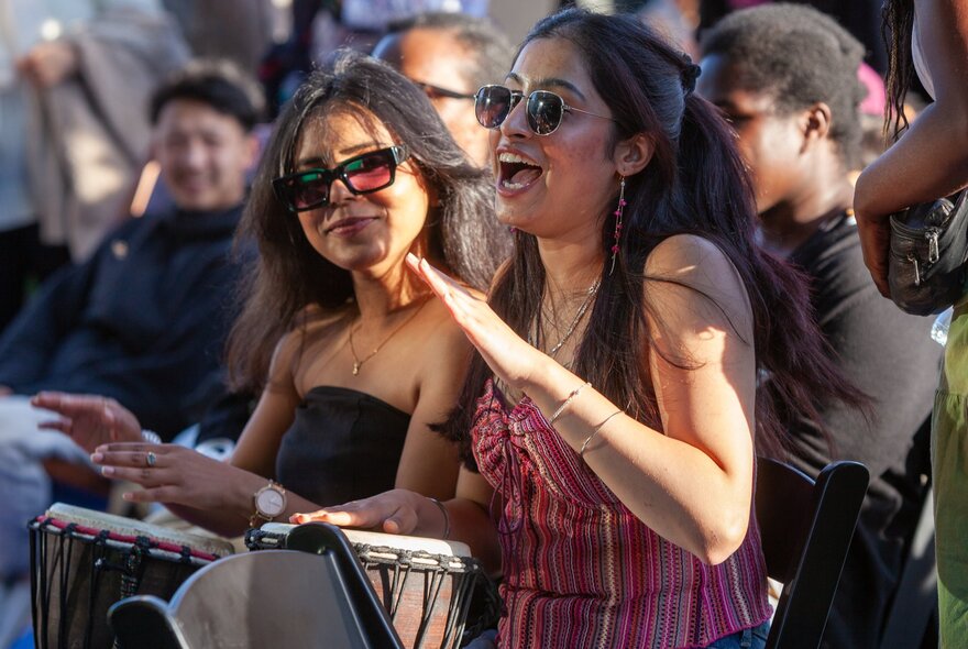 A group of people drumming at a festival, the central figure is singing. 