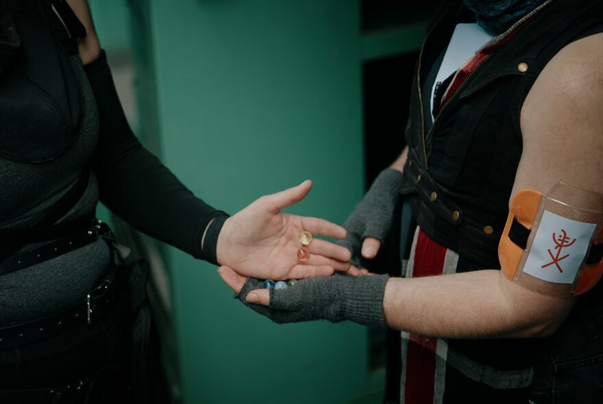 Person handing glass balls to another person wearing gloves and a team armband.