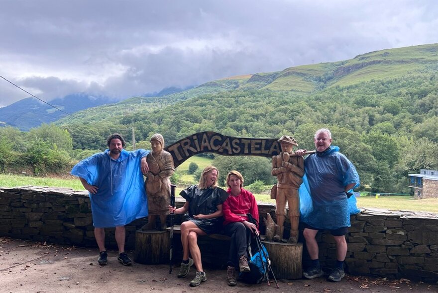 A group of walkers resting in Triacastela, Spain, during their journey on the Camino de Santiago, with green hills in the background.