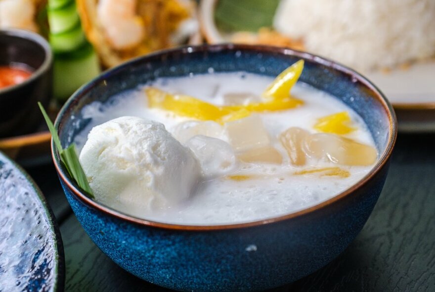 A blue ceramic bowl filled with a dessert, slices of mango and icecream.