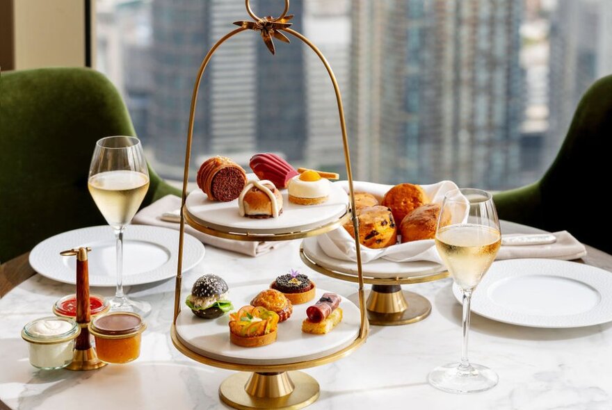 A linen covered dining table set out with high tea offerings including sweet and savoury food, glasses of sparkling wine and white plates.