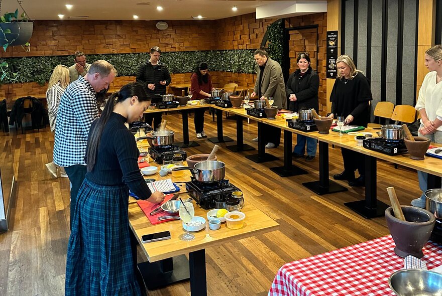 A group of people standing around a U-shaped timber workbench, learning to make Italian antipasto.