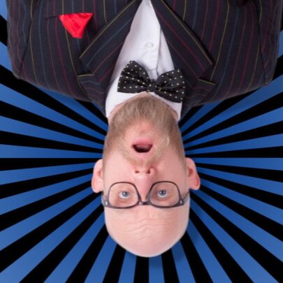 Bald man with spectacles and beard, wearing bow tie and jacket, pictured upside down.