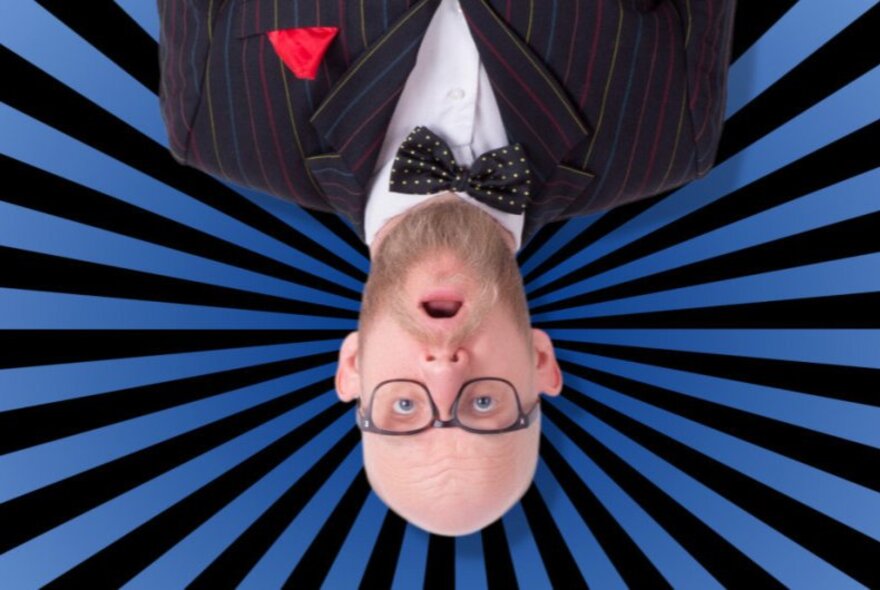 Bald man with spectacles and beard, wearing bow tie and jacket, pictured upside down.