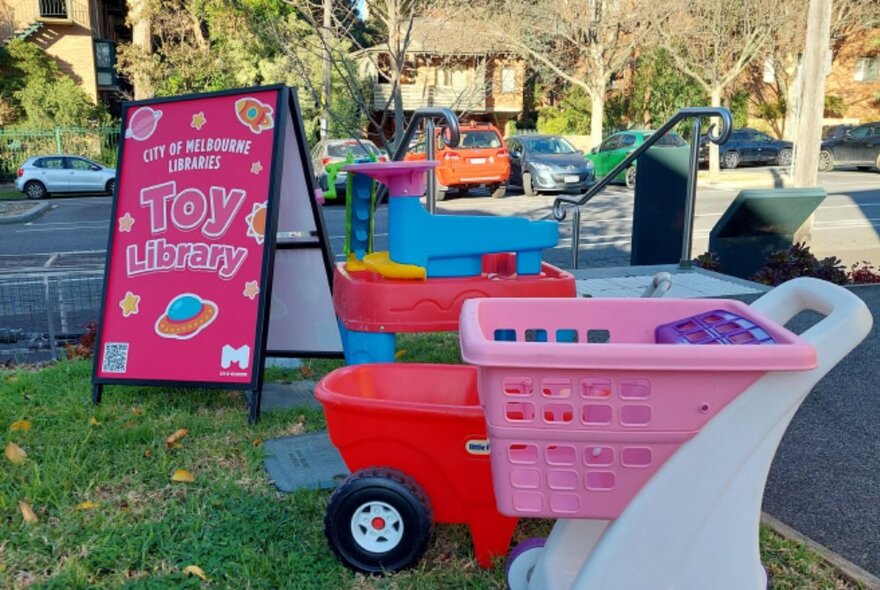 The grassy area outside the toy library in Carlton, with some small toys on display and a sandwich board that has the words TOY LIBRARy written on it.