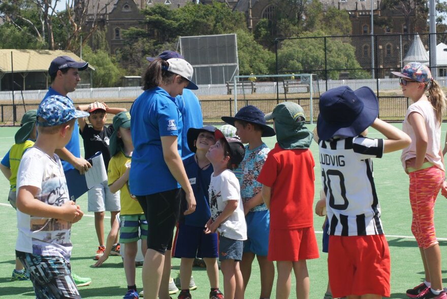 Children standing in a line and interacting with an adult outdoors on a green lawn.