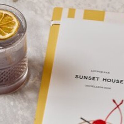A cocktail on a table next to a menu.