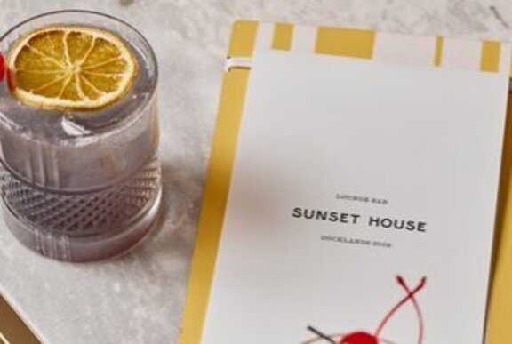 A cocktail on a table next to a menu.