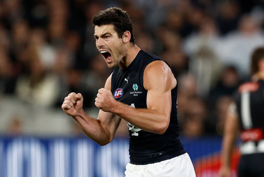 A Carlton AFL football player making fists and yelling during a game.