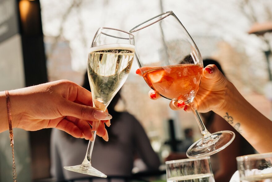 Two women's hands holding glasses, one with sparkling wine and the other an Aperol spritz.