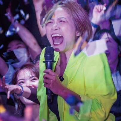 A comedian holding a microphone, surrounded by people waving their hands, screaming.