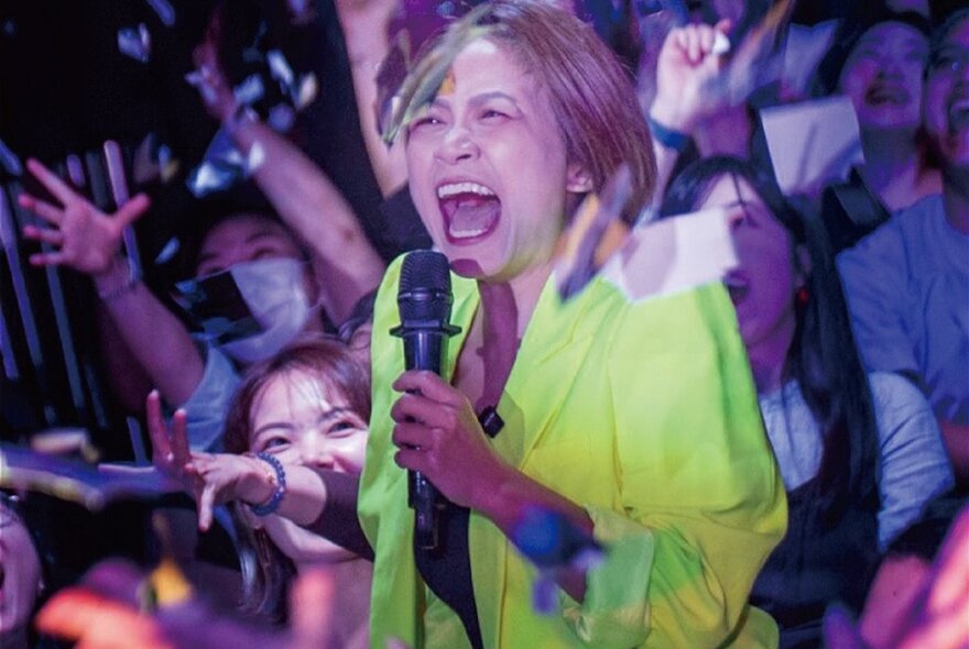 A comedian holding a microphone, surrounded by people waving their hands, screaming.