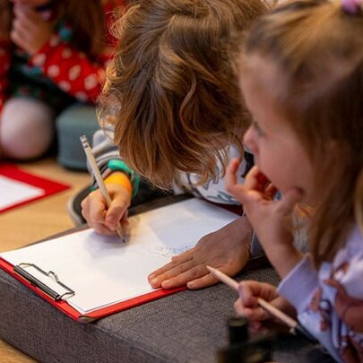 Three young children on the floor, each with a pencil and a clipboard.