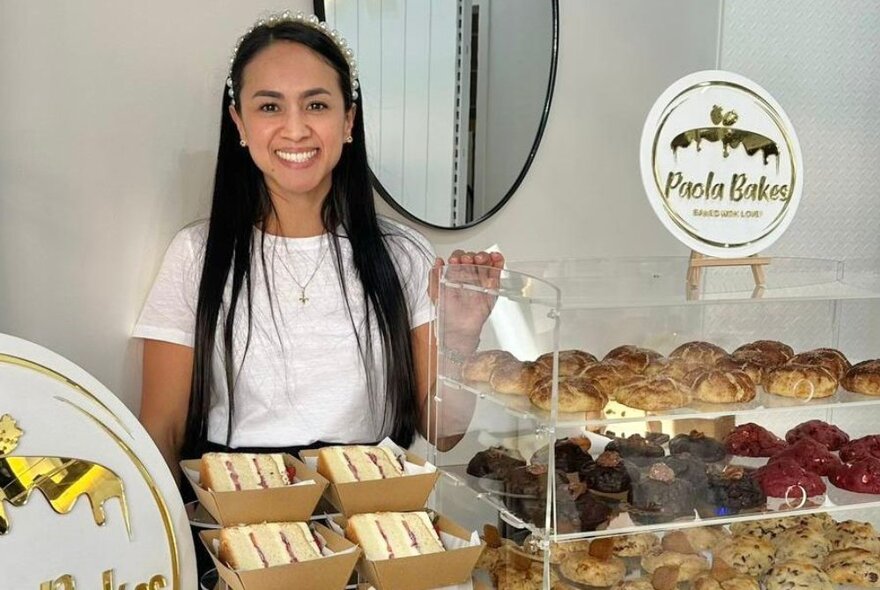 A woman standing behind a glass cabinet of pastriesnext to slices of cake in cardboard trays.