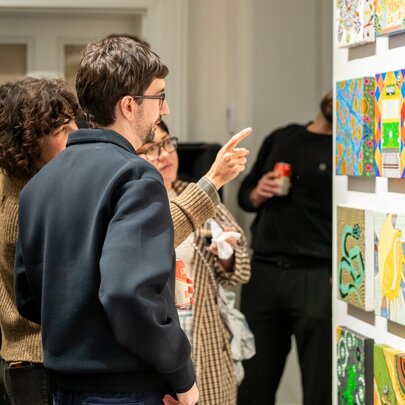 People in a gallery interacting while looking at artworks on a wall.