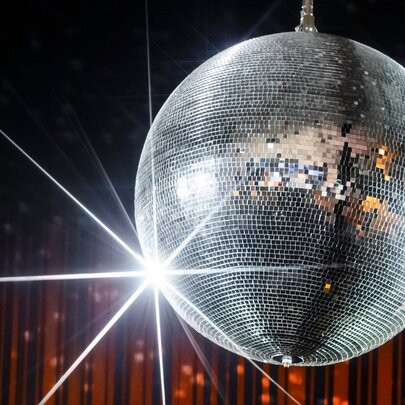 Silver glitter ball in front of red sparkly curtain.