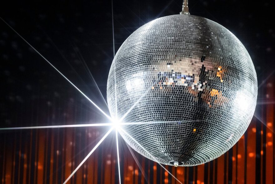 Silver glitter ball in front of red sparkly curtain.