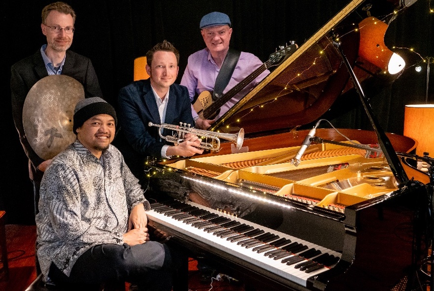 Jazz musicians gathered around a grand piano, with pianist seated at the piano, other musicians holding instruments.