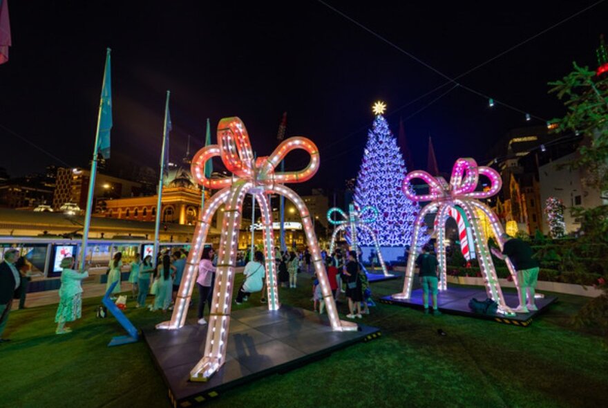 Groups of people standing giant Christmas bells with a big Christmas tree.