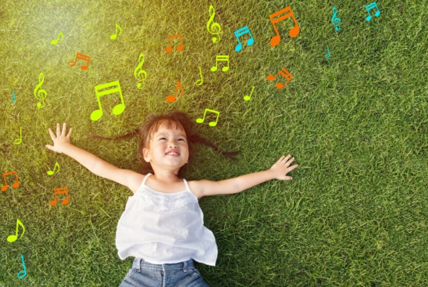 A little girl laying on grass with her arms outstretched and music note graphics floating around her head. 