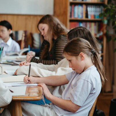 Young teens writing on notebooks or into laptops around a table, as part of a creative writing workshop in a studio setting.