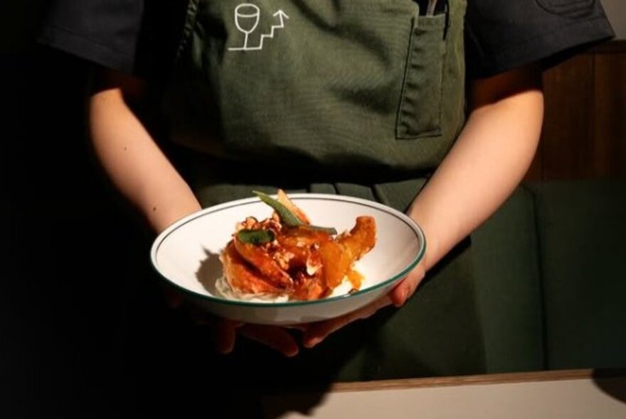 A waiter wearing an olive green apron holding a plate of food in their hands.